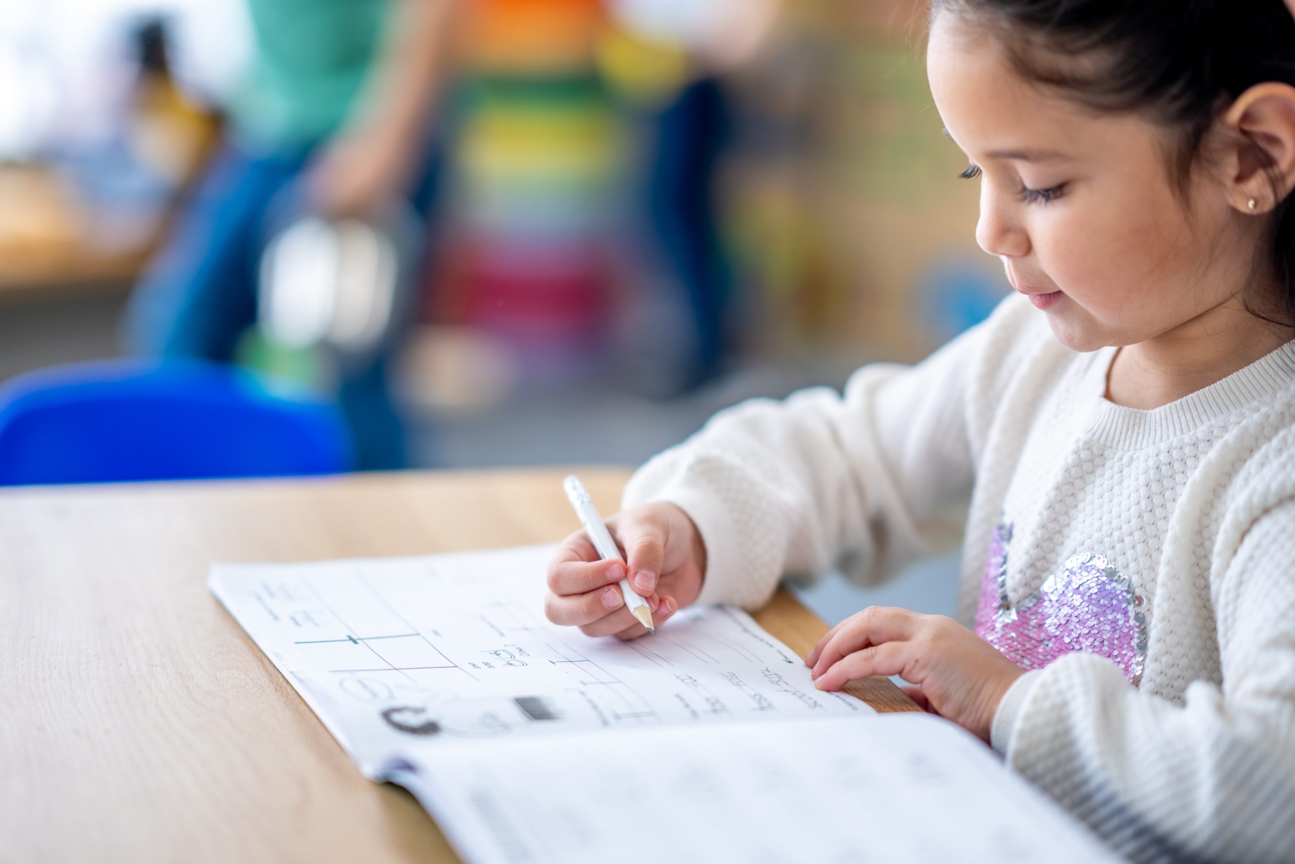 A sweet mixed race elementary student sits at her desk as she works through a writing workbook independently.