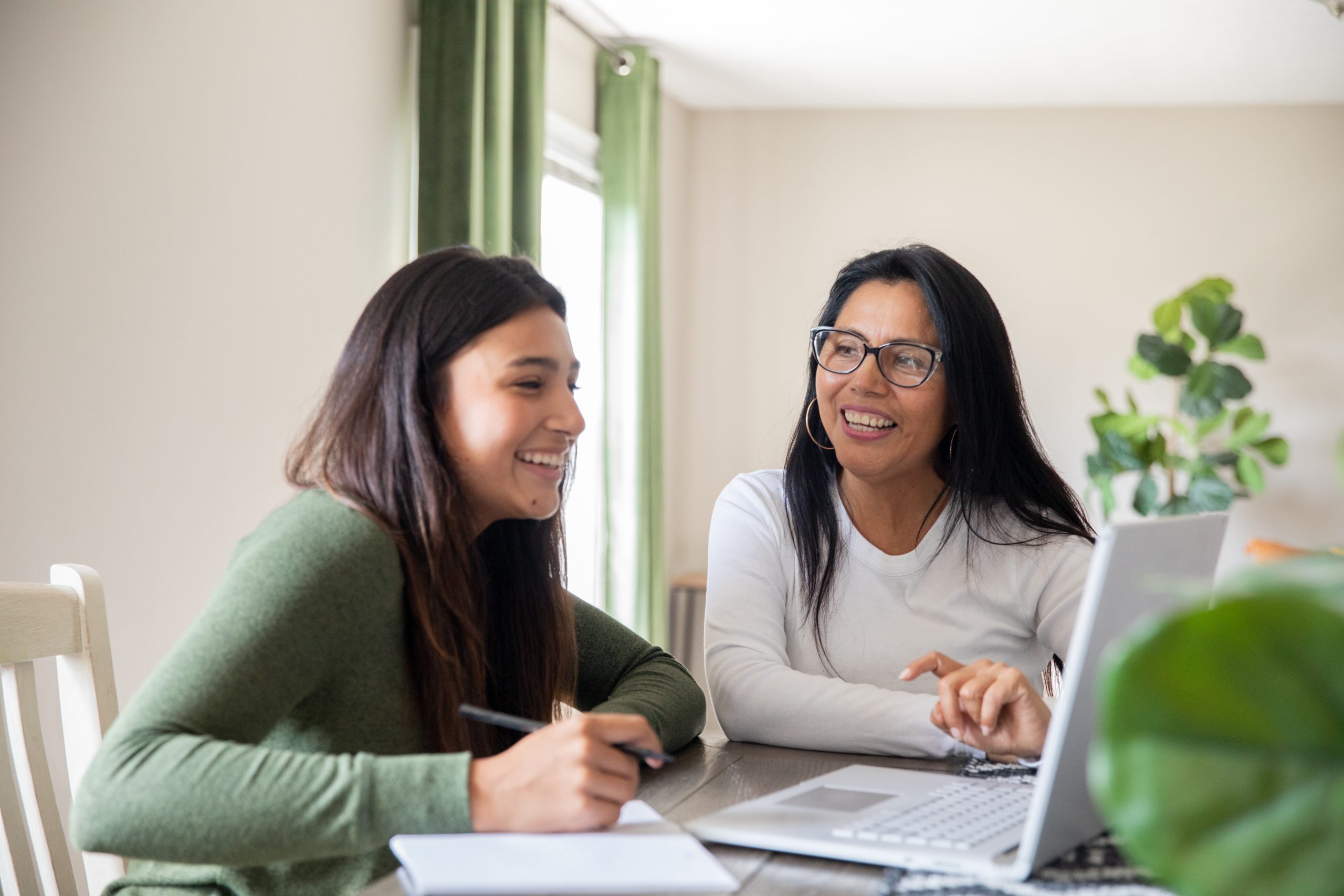Using their home computer, a mother aids her teenage daughter in completing a virtual high school task.