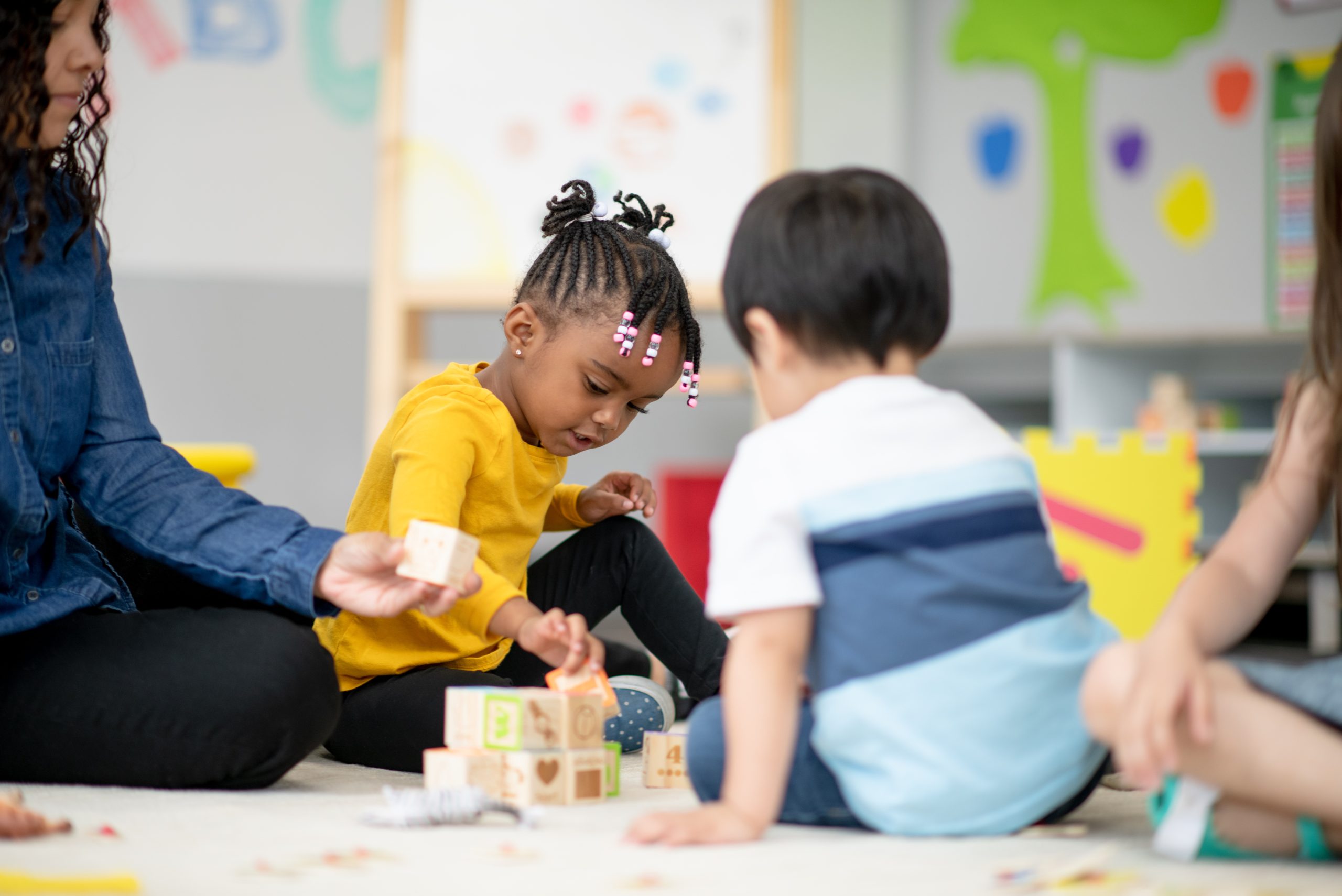 A diverse group of kids sit on the carpet and play with each other.