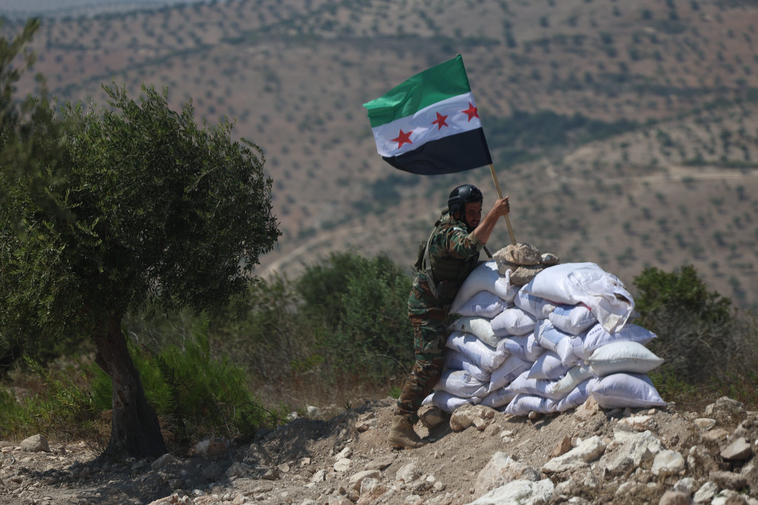 AFRIN, SYRIA - AUGUST 08: A graduating recruit plants a flag during battle simulation training on August 08, 2024 in Afrin, Syria. Two hundred recruits of the Samarkand Brigade, apart of the Turkish-backed, Syrian National Army graduated after more than a month of intensive training. The graduation day included a simulation of real life raids and battle situations , including the detonation of mines, heavy machine gun use, assault raid tactics and military vehicle training.  (Photo by Ghaith Alsayed/Getty Images)