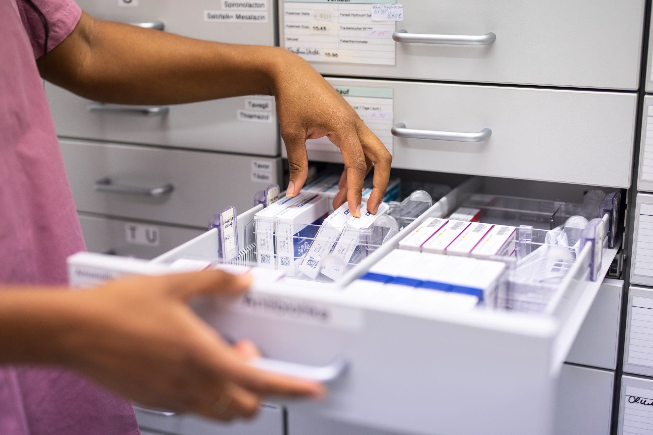 Close-up of a female pharmacist searching for prescription medicine in storage rack. Woman hands looking for medicine in a storage rack in the hospital pharmacy store.