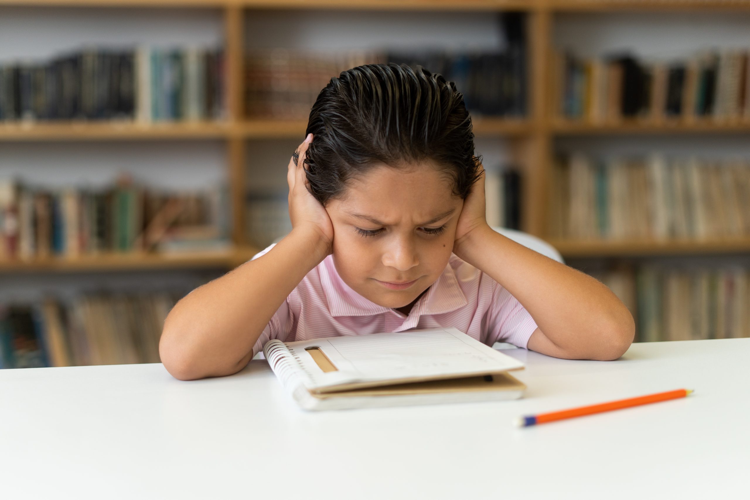 A little boy in class with his head between his hands and looking confused.