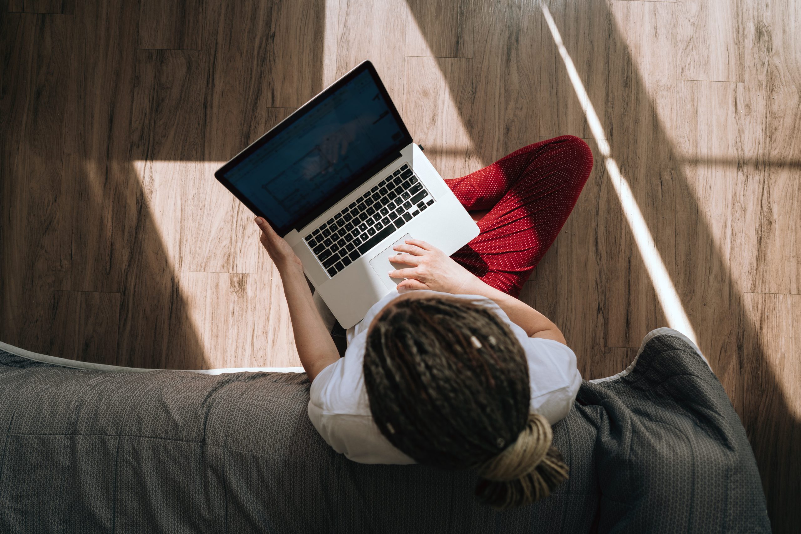 Top and back view of a woman in home clothes sitting on the floor typing on a laptop. Work at home. Portrait of a dreadlocks braid woman.