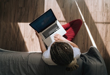 Top and back view of a woman in home clothes sitting on the floor typing on a laptop. Work at home. Portrait of a dreadlocks braid woman.