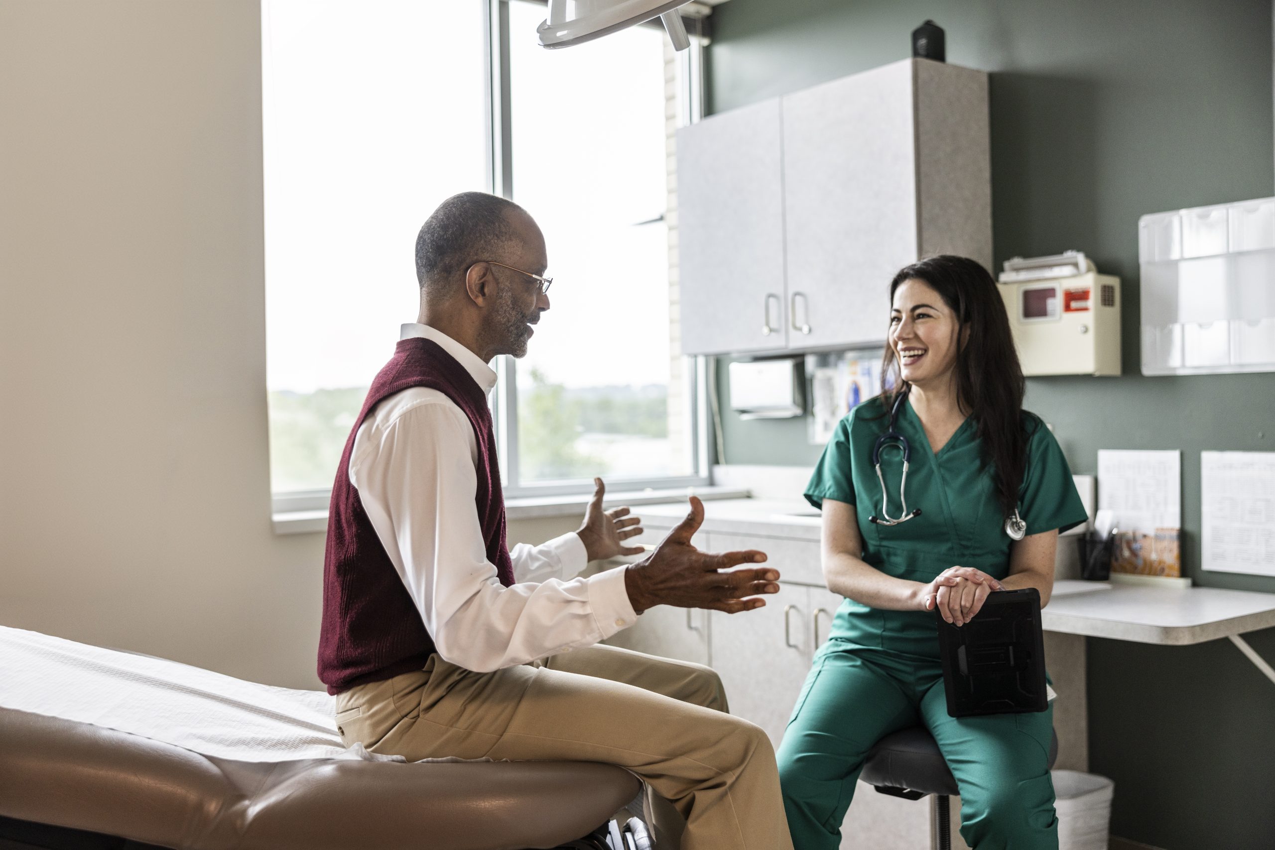 Female doctor talking with senior male patient in exam room