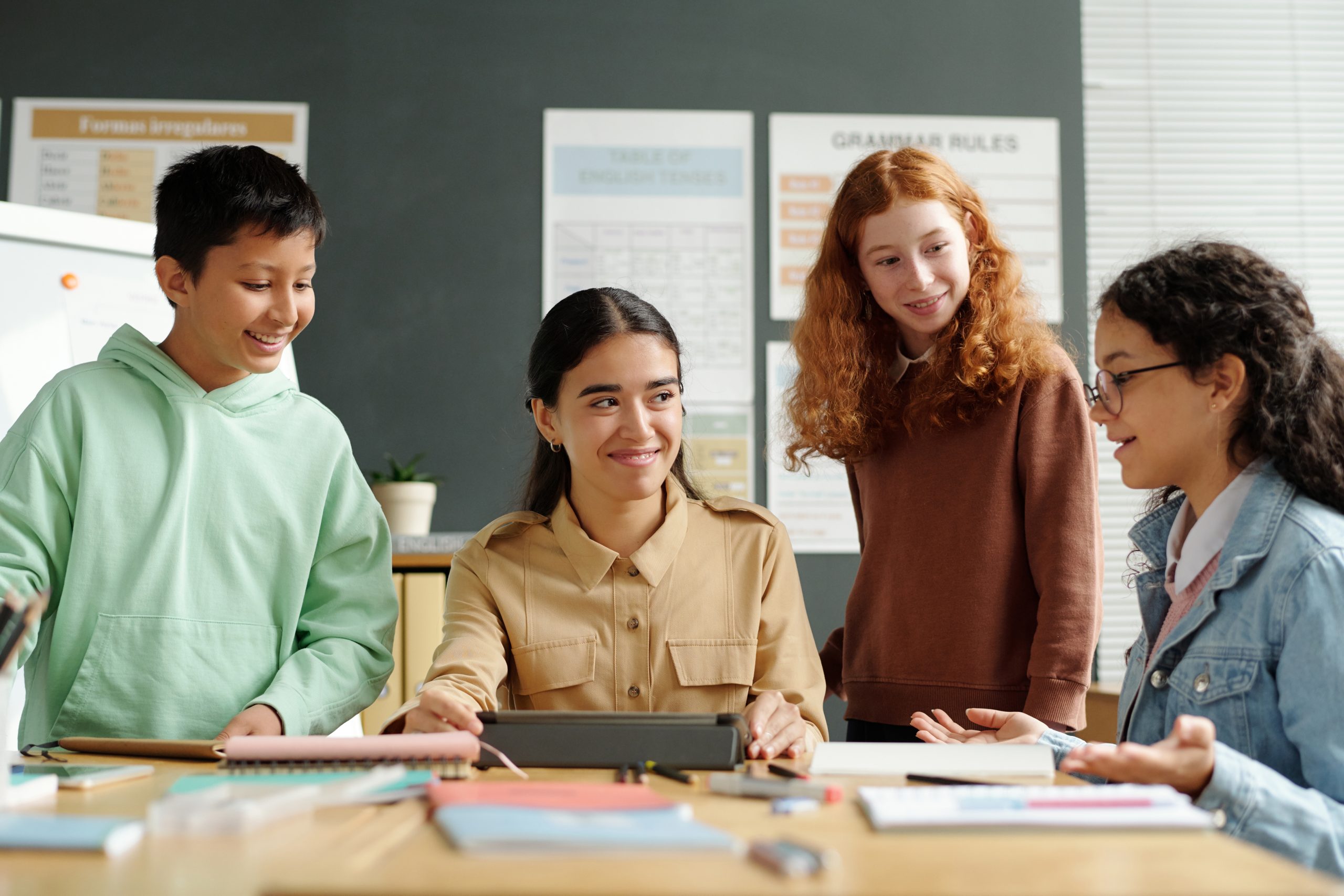 Group of learners and their teacher listening to clever schoolgirl explaining grammar rule at lesson of English language while looking at her
