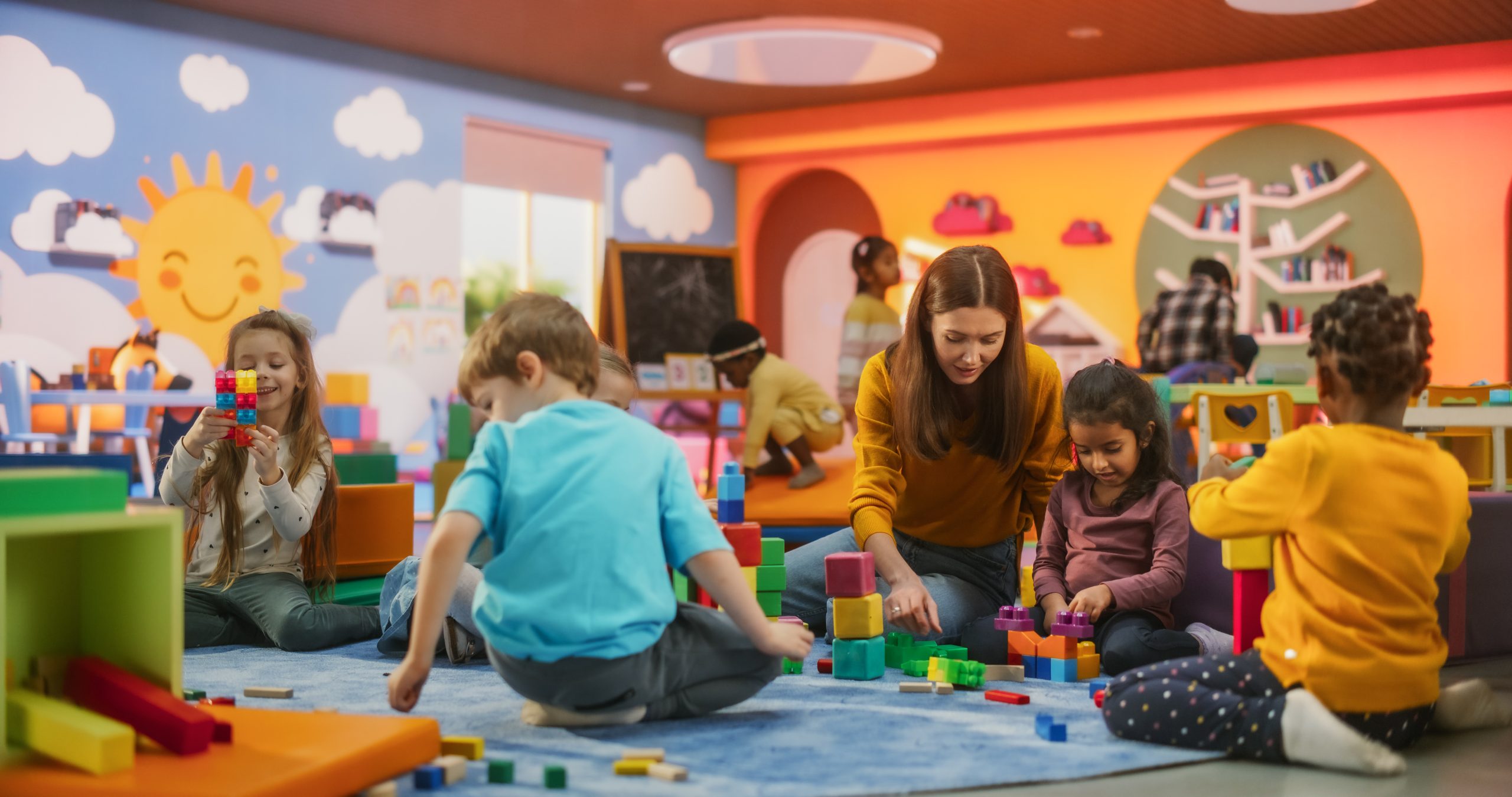 Cheerful Diverse Kids Playing with Colorful Building Block Toys in Kindergarten. Group of Multiethnic Boys and Girls Playing Together with a Female Teacher in a Modern Daycare Center