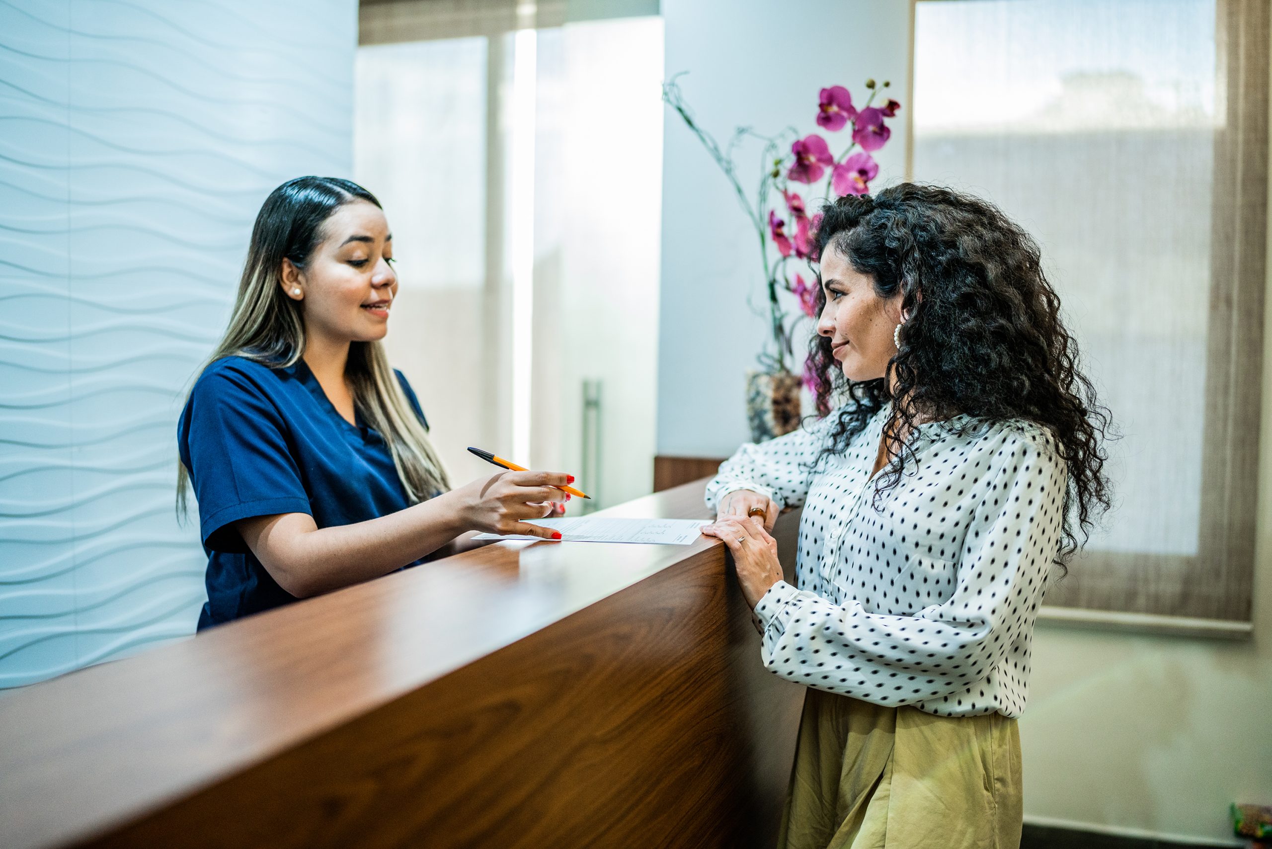 Mid adult woman talking with receptionist at the reception desk of the dentist's office