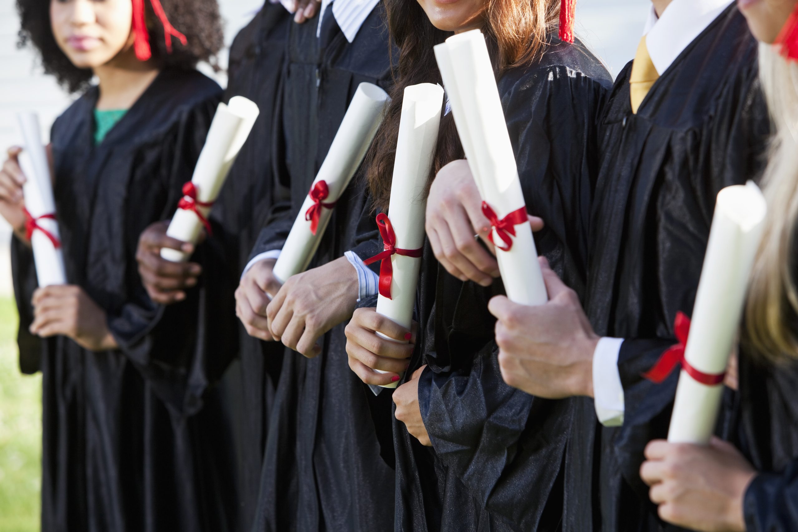 Cropped view of multi-ethnic friends graduating together, in cap and gown.   Shallow DOF. focus on girl in middle.