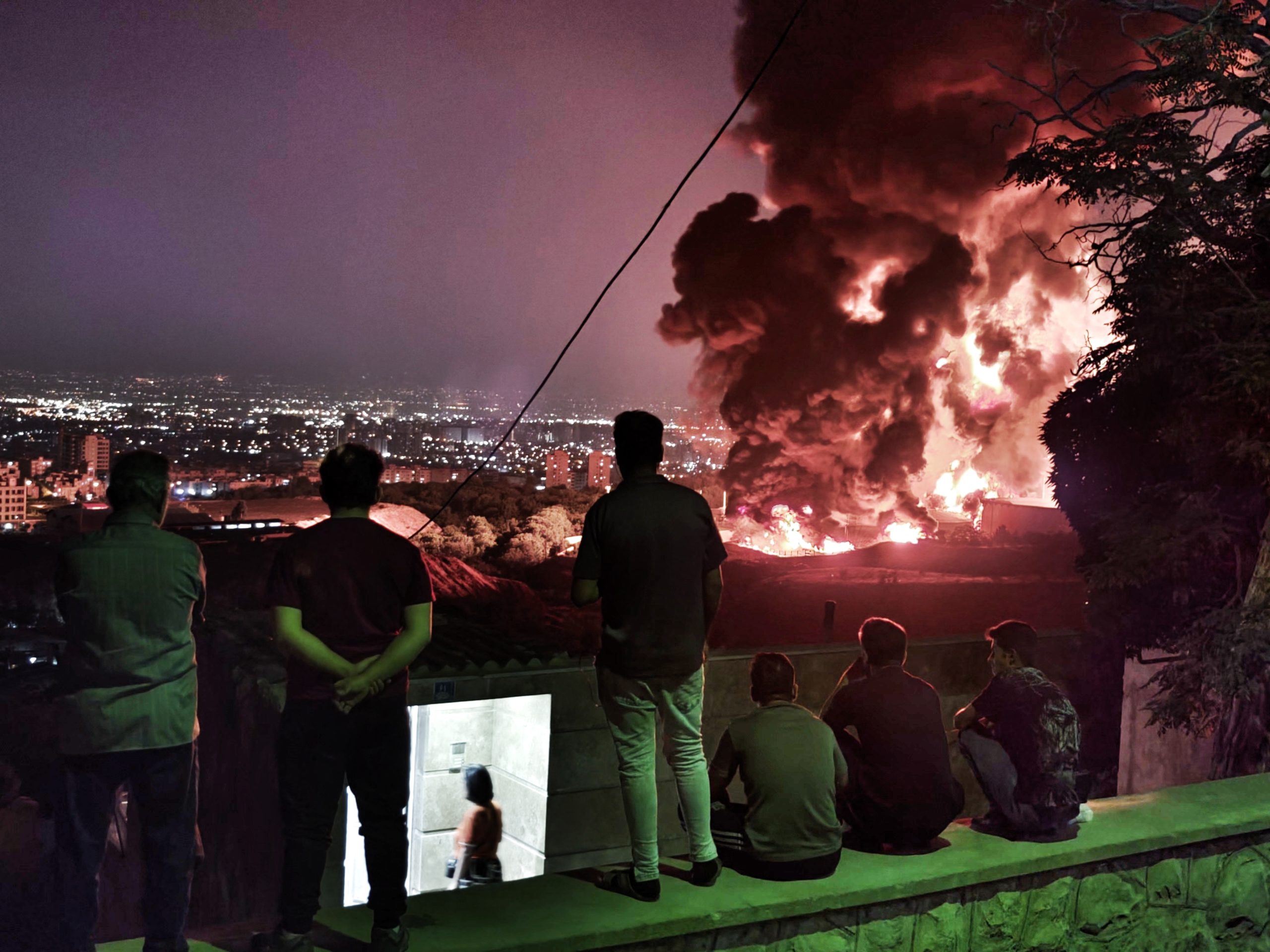TEHRAN, IRAN - JUNE 15: People observe fire and smoke from an Israeli attack on the Shahran oil depot on June 15, 2025 in Tehran, Iran. Iran's foreign minister said the country would respond 