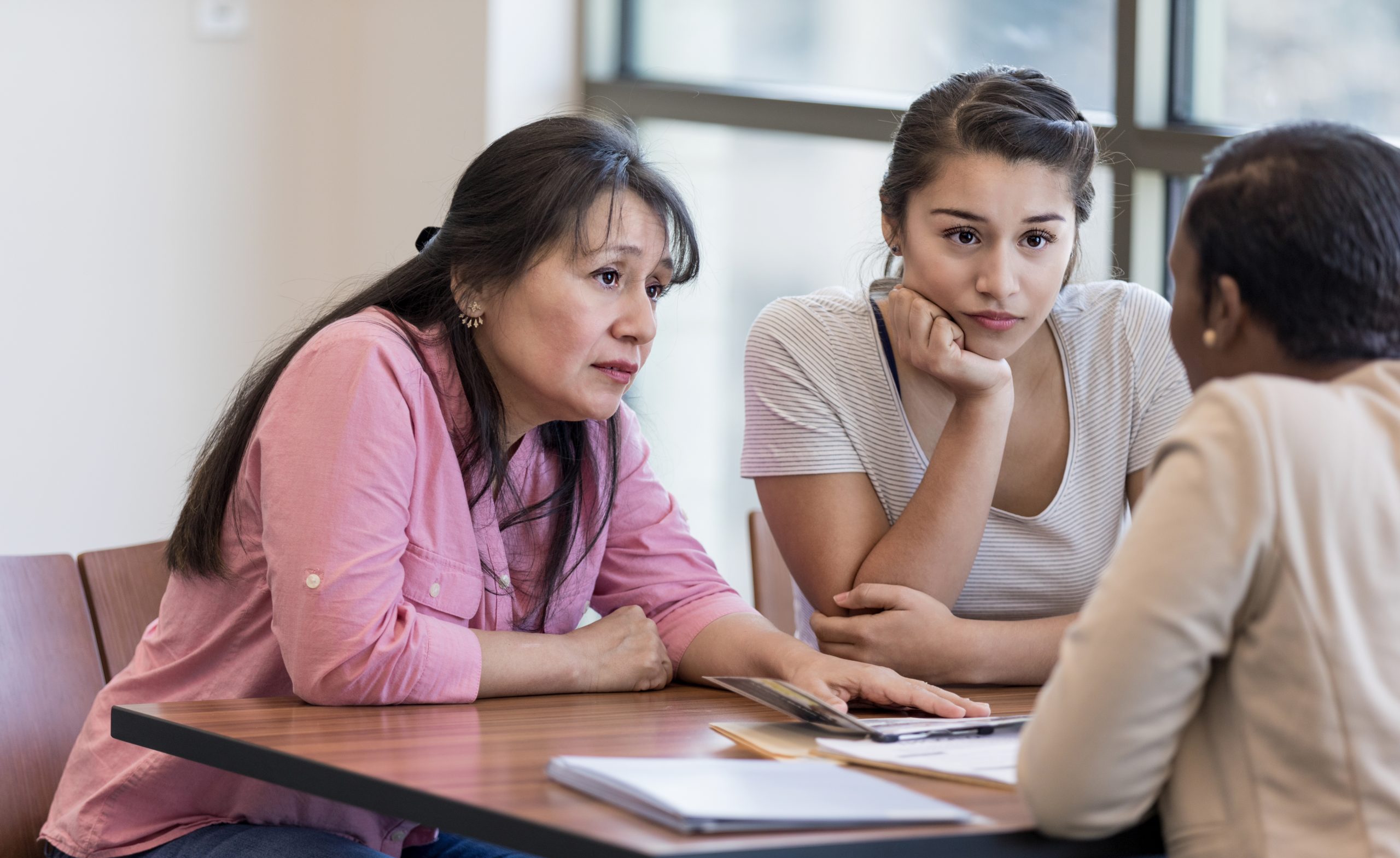 Concerned mother and daughter talking to loan officer at bank.