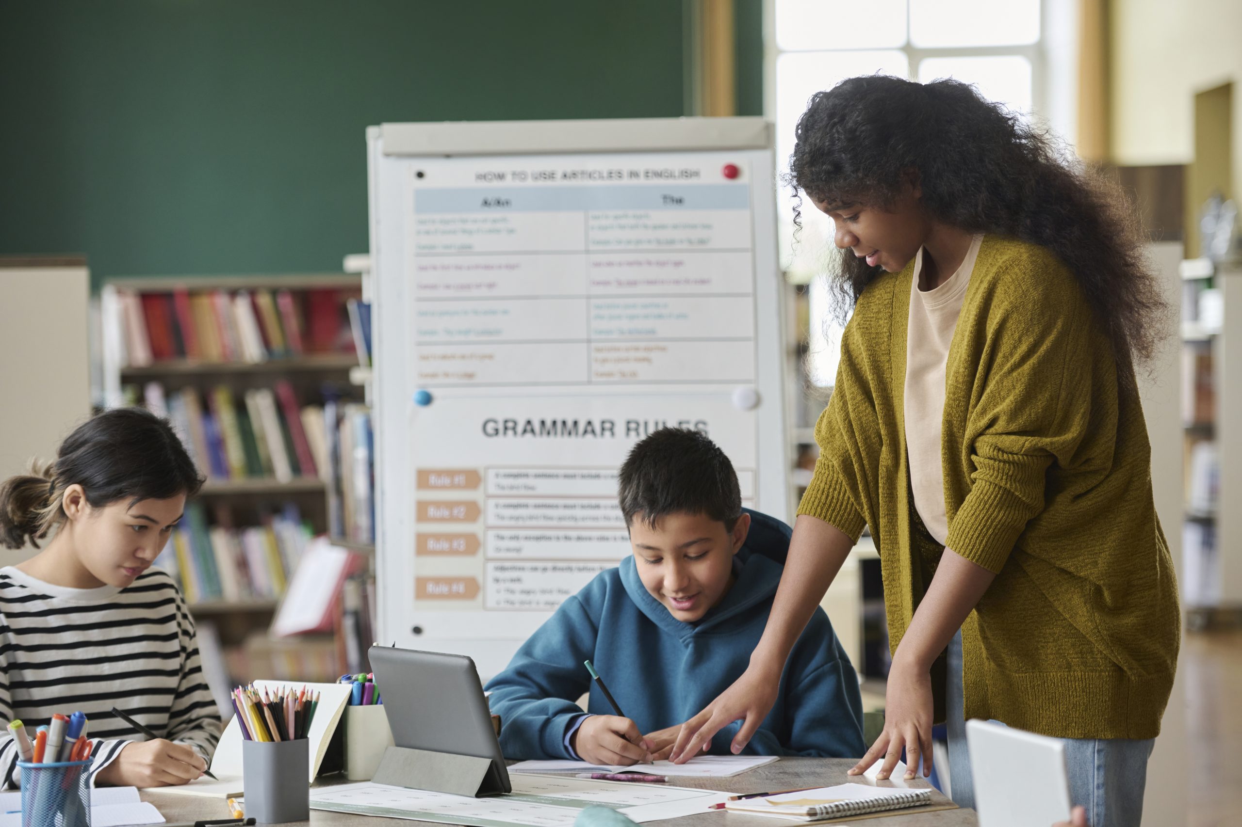 Girl assisting classmates in a language class with grammar rules in the background