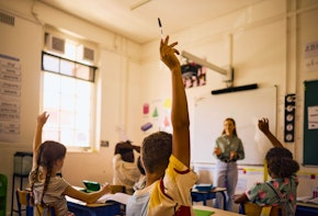 Diverse group of elementary school students actively participating in class, raising hands to answer teacher's question
