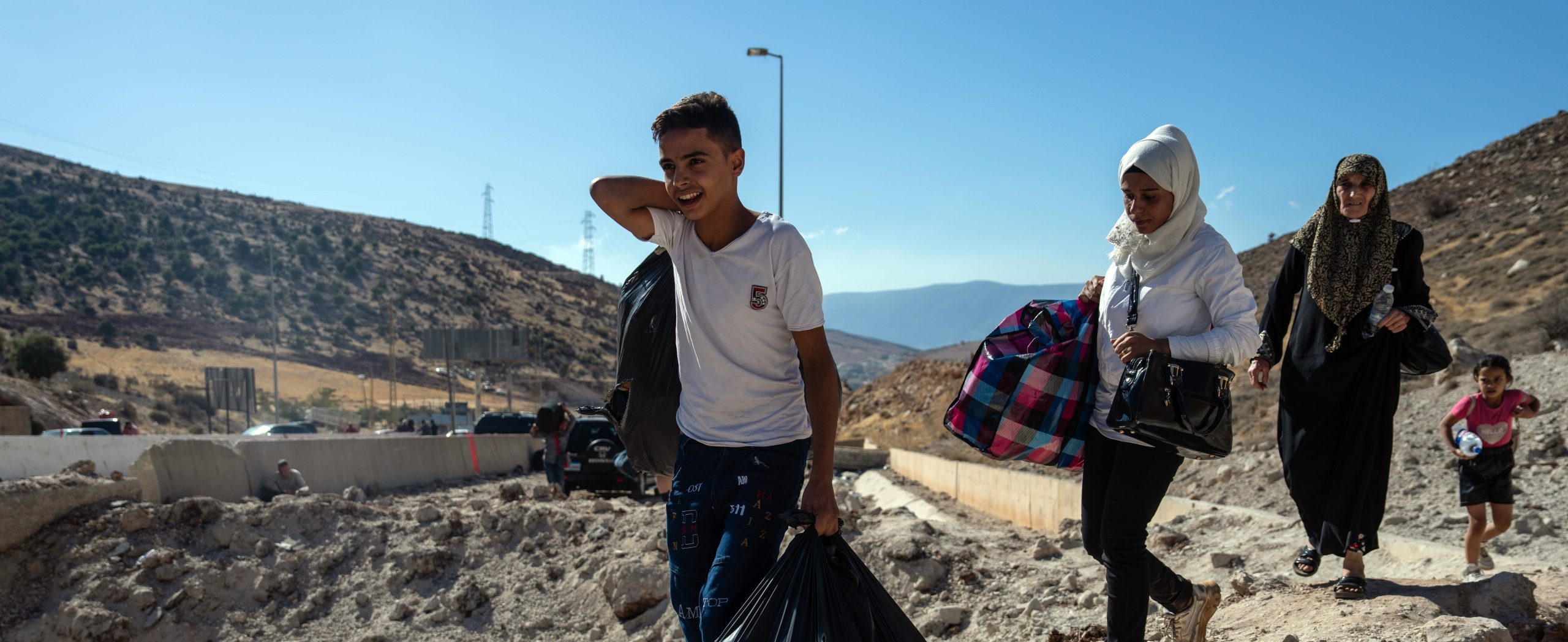 MASNAA, LEBANON - OCTOBER 5: People carry baggage around the crater from an Israeli air strike as they make their way across the border from Lebanon into Syria on October 5, 2024 in Masnaa, Lebanon. Israel continued airstrikes on Beirut and its southern suburbs as its military announced a ground offensive in Lebanon, part of what it said would be a 