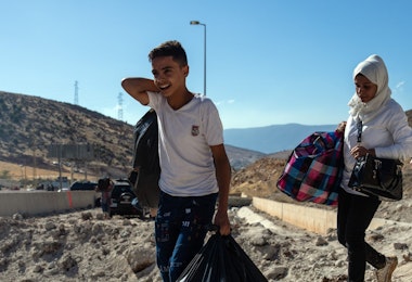MASNAA, LEBANON - OCTOBER 5: People carry baggage around the crater from an Israeli air strike as they make their way across the border from Lebanon into Syria on October 5, 2024 in Masnaa, Lebanon. Israel continued airstrikes on Beirut and its southern suburbs as its military announced a ground offensive in Lebanon, part of what it said would be a