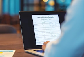 Businessman applying for unemployment benefits. He is filling in a form using a laptop computer in an office