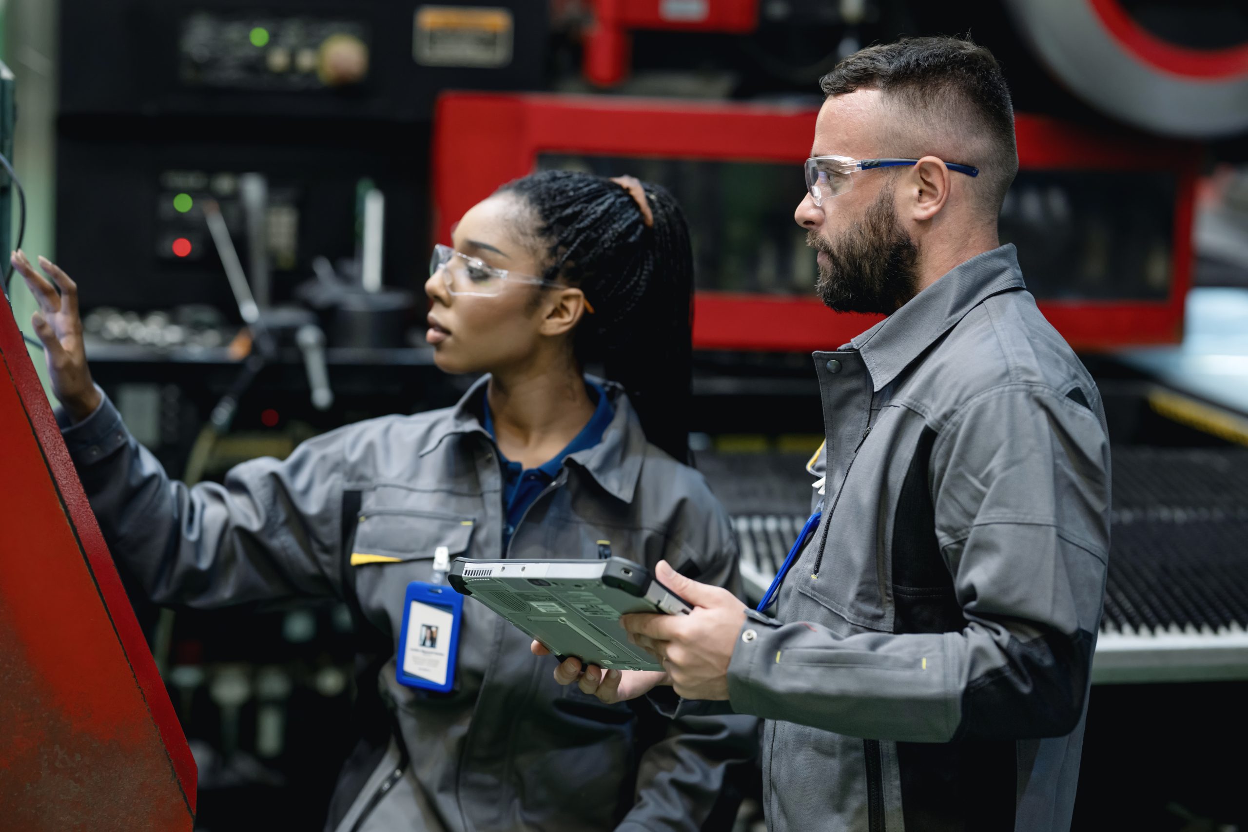 Continuous Manufacturing Improvement Can Improve Engineering Product Quality with Total Quality Management (TQM). A male industrial engineer advises a female engineer about the automatic punching machine control process for engineering parts production.
